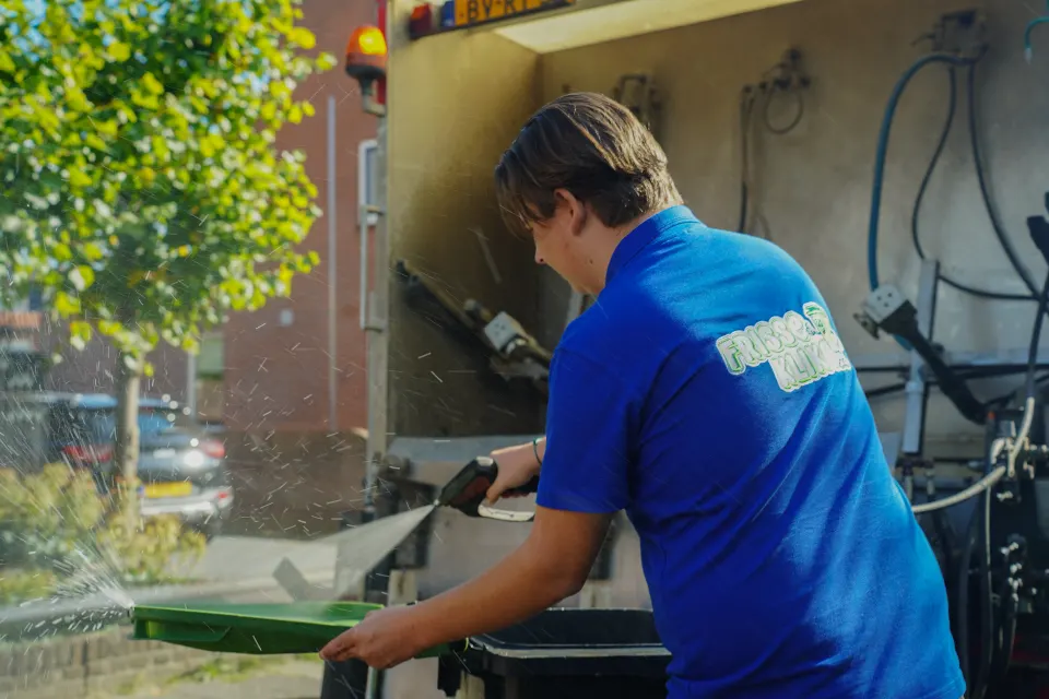 Medewerker maakt een groene container schoon bij de reinigingswagen.